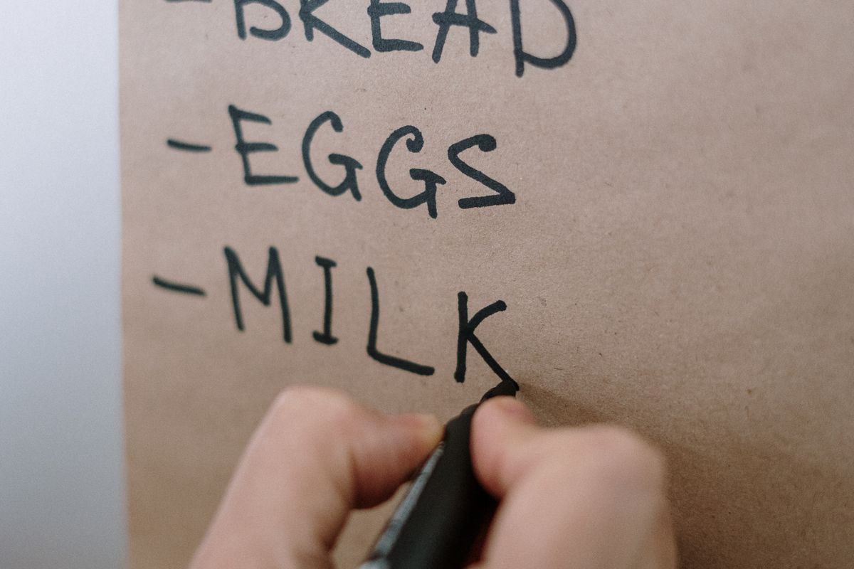 A hand writing bread, eggs and milk on a paper shopping list