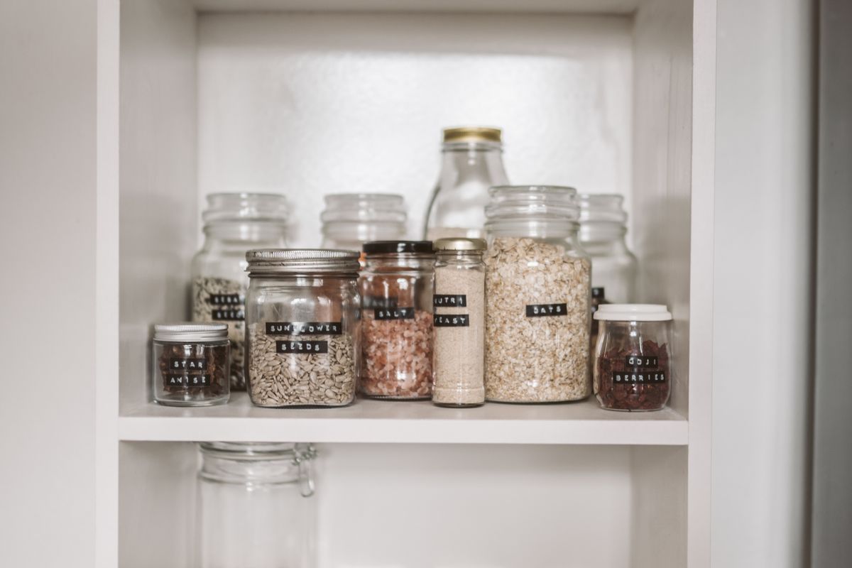 Labelled glass jars of oats, seeds and salt on a pantry shelf
