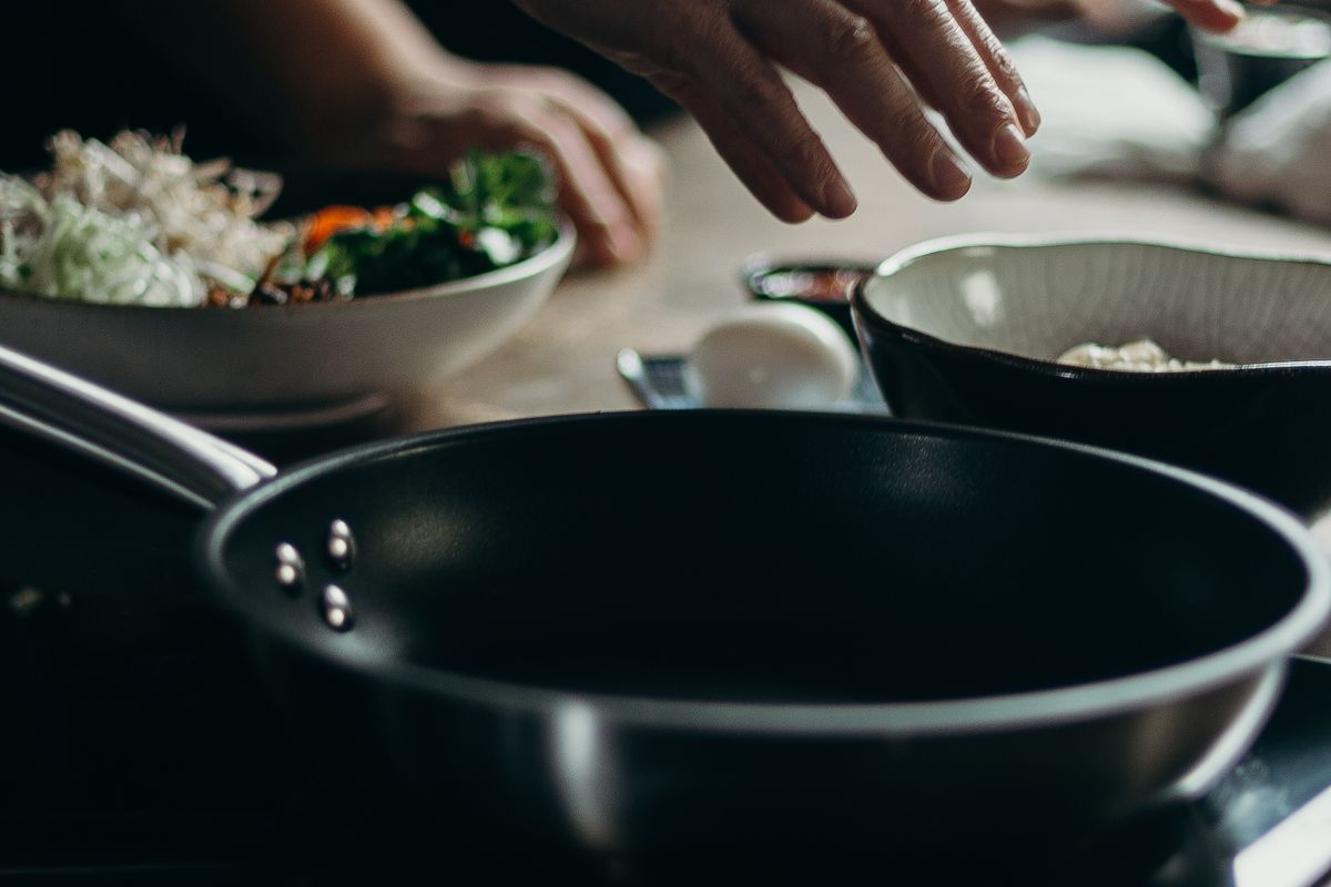 Hands seasoning food beside a pan and bowls of prepared vegetables