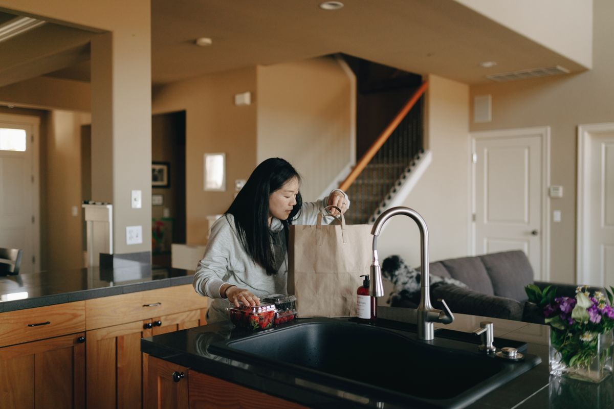 A person unpacking a paper grocery bag at a kitchen counter