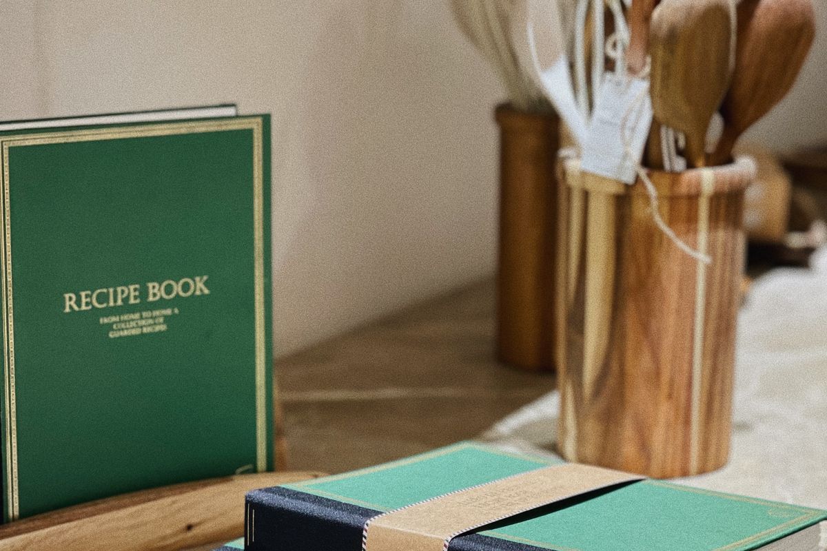 A green recipe book standing beside a jar of wooden utensils