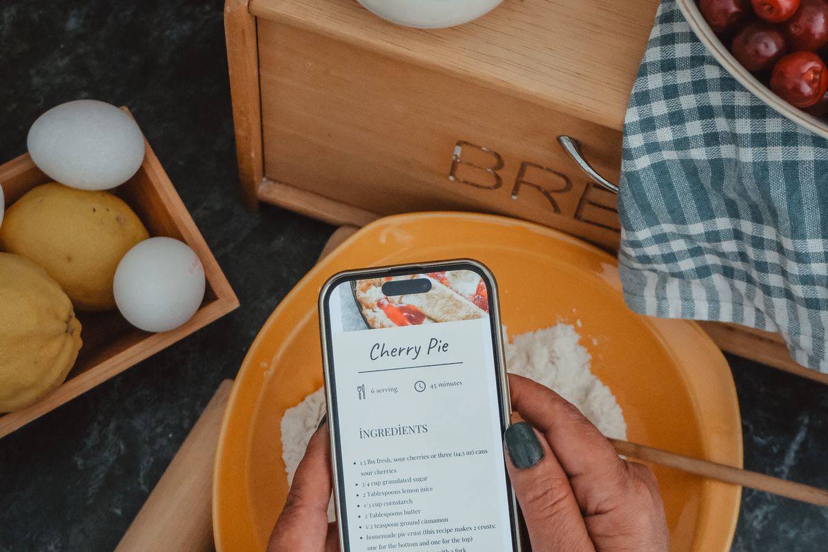 A phone showing a cherry pie recipe, held over a bowl of flour