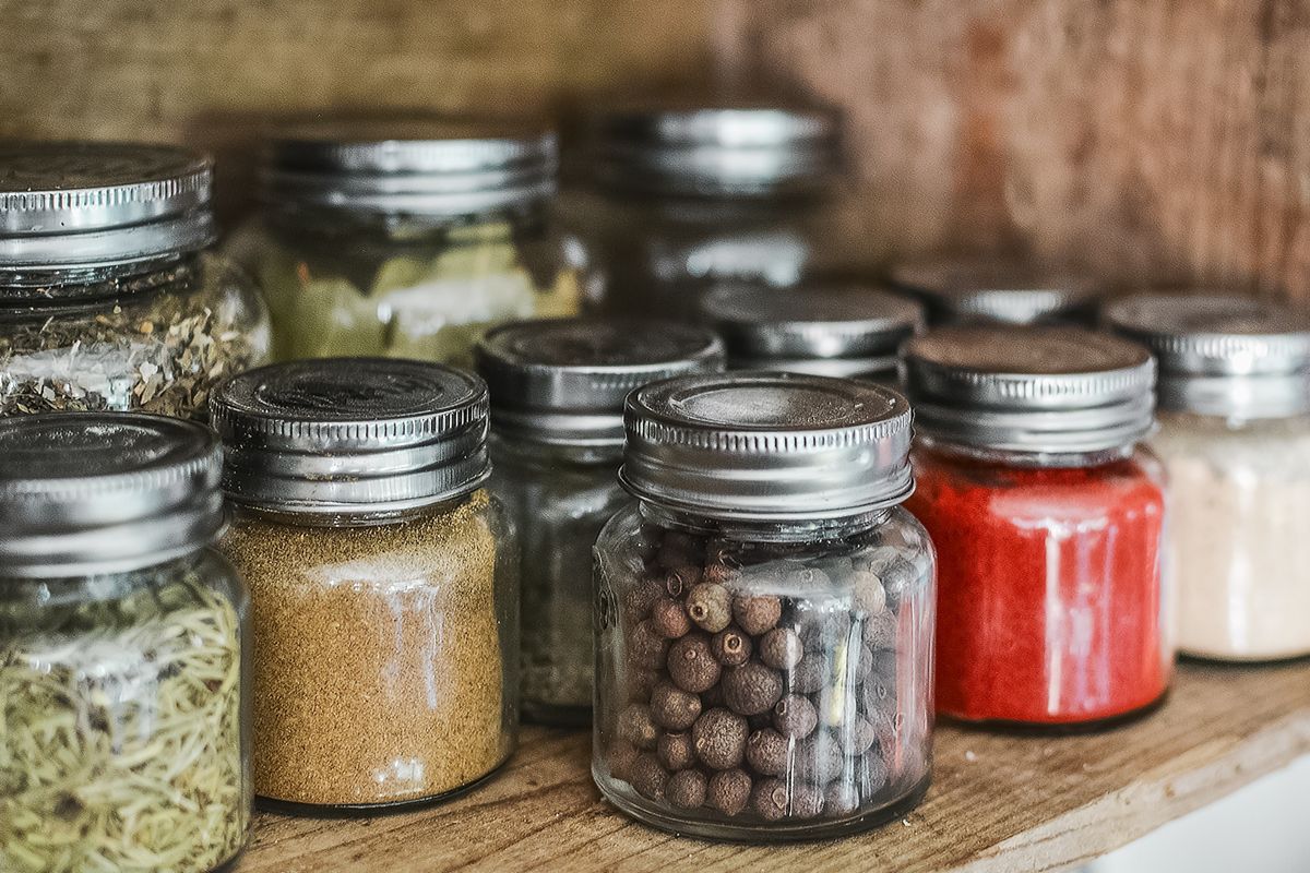 Rows of small glass spice jars lined up on a wooden shelf
